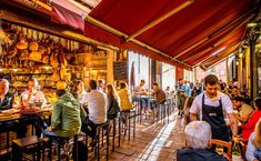 many people are sitting at tables in a restaurant with red awnings over them