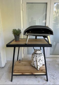 an outdoor bbq grill sitting on top of a wooden shelf next to a potted plant