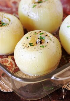 three peeled onions in a glass dish with seasoning sprinkled on the tops