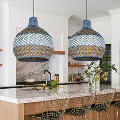 a kitchen island with four chairs and two pendant lights hanging over the counter top in front of it