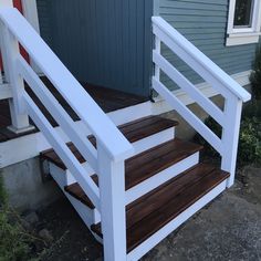 a white wooden stair case next to a blue door and green siding on a house