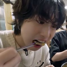 two young men eating food from bowls in a restaurant while one man looks at the camera