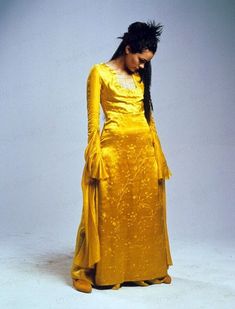 a woman in a yellow dress with long black hair and braids standing against a white background