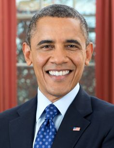 a man in a suit and tie smiling for the camera with red curtains behind him