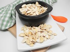 a black bowl filled with pumpkin seeds on top of a white plate next to a wooden spoon