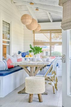 a table and chairs on a porch with hanging lights above it, next to a bench