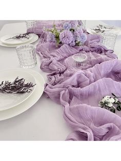 the table is set with purple flowers and glassware, plates and napkins on it