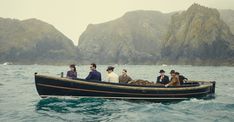 a group of people riding on the back of a boat in the ocean next to mountains