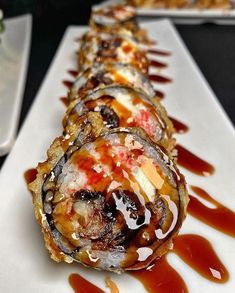 there are many sushi rolls on the plate with sauce drizzled around them