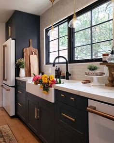 a kitchen with black and white cabinets, wood flooring and yellow flowers on the counter