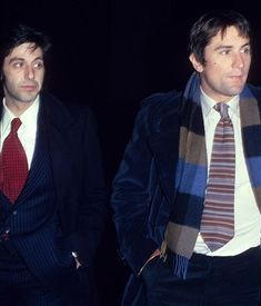 two men in suits and ties standing next to each other, one wearing a scarf