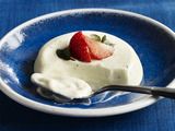 a small bowl filled with yogurt and a strawberry on top, sitting on a blue table cloth