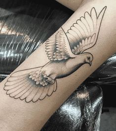 a black and white photo of a dove tattoo on the arm, with wings spread out