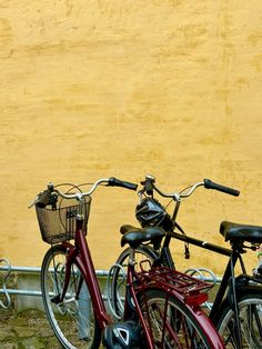 two bikes parked next to each other in front of a yellow wall