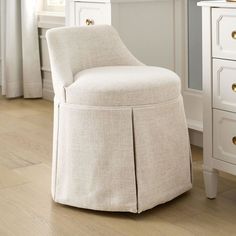 an upholstered chair sits in front of a white dresser with drawers on both sides