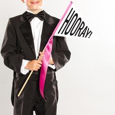 a young boy in a tuxedo holding a pink and white flag