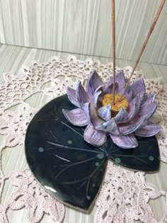 a purple flower sitting on top of a black piece of wood next to lace doily