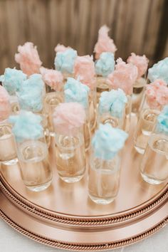 small desserts are arranged in glass vases on a gold platter with pink and blue frosting