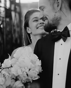 black and white photograph of bride and groom smiling at each other with flowers in front of them