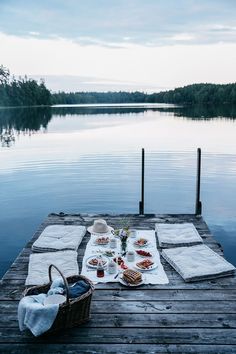 an outdoor picnic is set up on a dock by the water with food and drinks