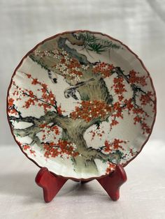 a white plate with an orange and red design on the front, sitting on a stand