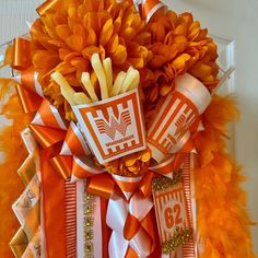 an orange and white wreath with feathers on the front door is adorned with flowers, ribbons, and stickers