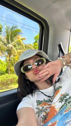 a woman sticking her tongue out in the back of a car while wearing sunglasses and a hat