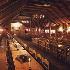 an empty dining hall with wooden tables and chairs, lit by candlelight from the chandeliers