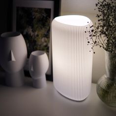 a white vase sitting on top of a table next to two small vases and a plant