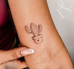 a woman's arm with a small tattoo of a cactus in a pot on it