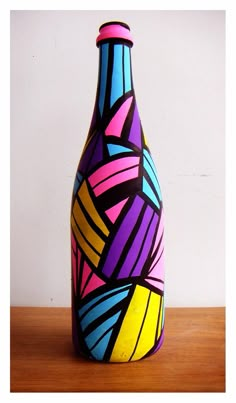 a colorful painted vase sitting on top of a wooden table next to a white wall