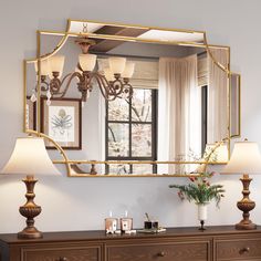 a large mirror sitting above a dresser with lamps on it's sides and a vase filled with flowers in front of it