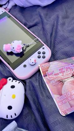 a hello kitty cell phone sitting on top of a bed next to a magazine and other items