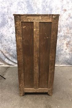 an old wooden cabinet sitting on top of a cement floor next to a white wall