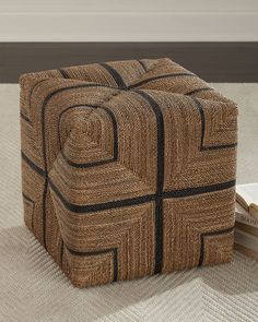 a brown and black square ottoman sitting on top of a white rug next to a book