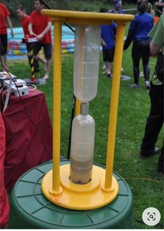 a yellow and green stand with a water bottle on it's top in the middle of a grassy area