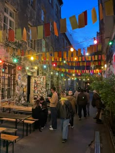 many people are walking down the street under some colorful flags and lights hanging above them