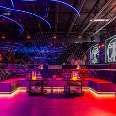 the interior of a nightclub with purple and blue lighting on the walls, tables and chairs