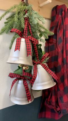 three white bells with red and black plaid ribbon hanging from the side of a wall