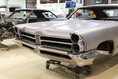 an old car is being worked on in a garage with other cars and machinery behind it