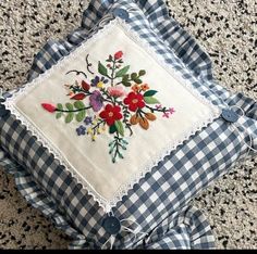 a blue and white checkered pillow on the ground with flowers embroidered on it's sides