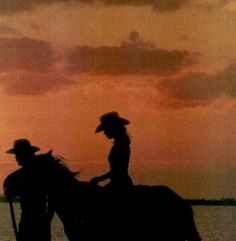 two people are riding horses in the water at sunset or dawn with clouds above them