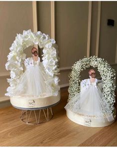 two figurines on display in front of a white wreath with baby's breath flowers