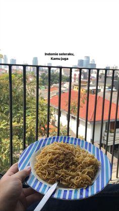 a person holding a plate of noodles on top of a balcony