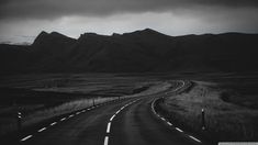 a black and white photo of a road in the middle of nowhere with mountains in the background