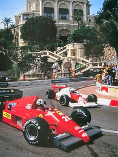 two racing cars driving down a race track in front of a large building with stairs