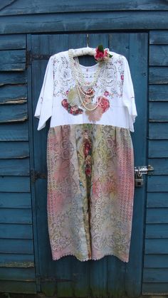 a white shirt with pink flowers on it hanging from a clothes line in front of a blue door