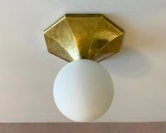 a white ball hanging from the ceiling next to a light fixture with a gold finish