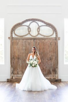 a bride poses in front of an old wooden door for her wedding photo shoot at the barn