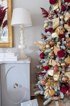 a christmas tree decorated with gold and red ornaments next to a white dresser in a living room